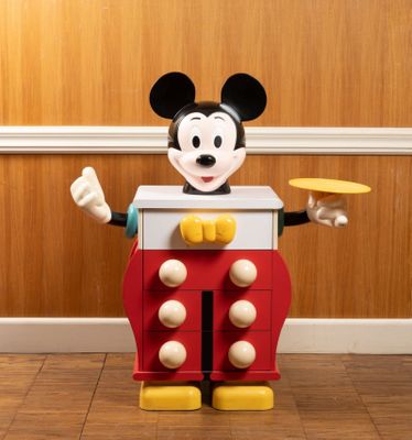 a mickey mouse toy standing on the floor with a frisbee in his hand