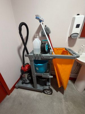 un chariot de nettoyage dans un coin des toilettes, sur lequel se trouvent une serpillière et un seau