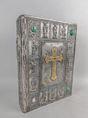 un vieux livre argenté avec une croix sur la couverture et une perle verte