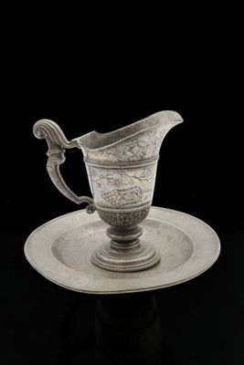 une assiette en argent ancien posée sur une soucoupe, sur fond noir
