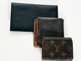 trois portefeuilles Louis Vuitton posés les uns à côté des autres sur une surface blanche
