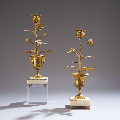 une paire de vases en or ornés de fleurs, posés sur des socles en marbre, sur fond gris
