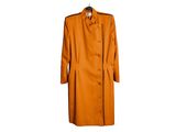 Un manteau orange est suspendu à un cintre accroché à un mur blanc.