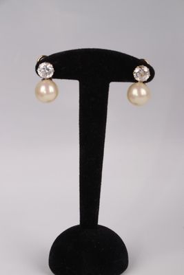 une paire de boucles d'oreilles en perles et diamants posée sur un présentoir noir