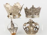 three silver crowns are on a clear stand on a white surface