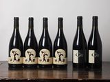 six bouteilles de vin sont posées sur une table en bois devant un mur blanc