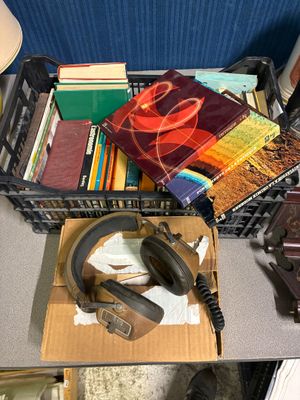 des livres et un casque audio posés sur un bureau où se trouvent une horloge et un téléphone