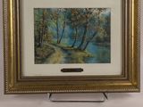 an oil painting of a river and trees in a gold frame on a white wall