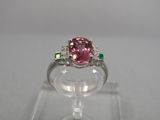 un gros plan d'une bague sertie d'un diamant rose et d'une émeraude, posée sur un socle transparent