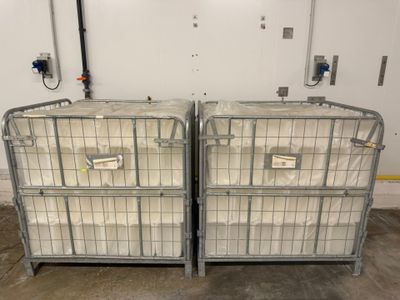 deux grandes cages métalliques recouvertes de sacs en plastique, dans un entrepôt
