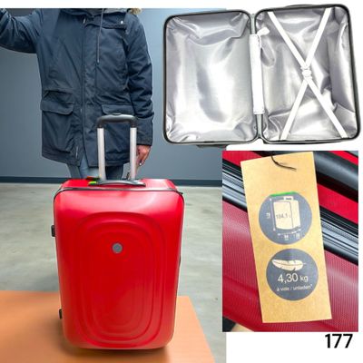 un homme debout à côté d'une valise rouge sur laquelle est accrochée une étiquette
