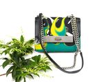a close up of a purse and a plant on a white surface