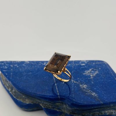 an image of a gold ring with a smoky quartz stone on a blue stone