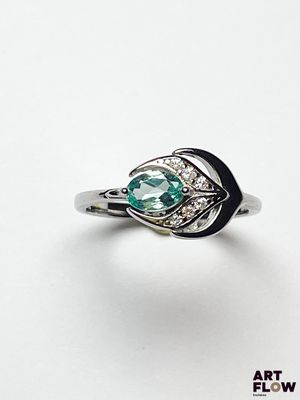 un gros plan d'une bague posée sur une surface blanche, ornée d'une pierre verte