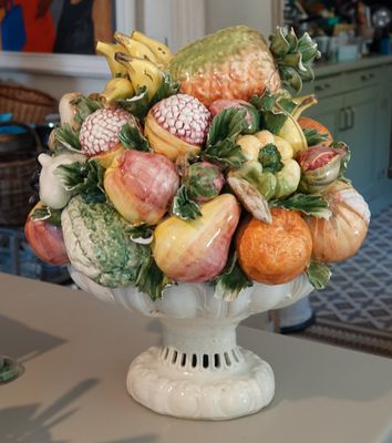 un vase blanc rempli de fruits et de légumes posé sur une table