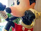statue of mickey mouse holding a baseball bat in front of a plant