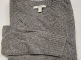Le pull est gris et comporte une étiquette blanche.