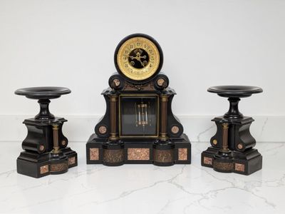 trois horloges noires et dorées posées sur une table en marbre