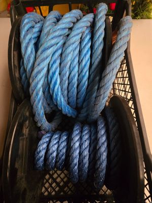 un panier noir rempli de corde bleue, à côté d'un tas de cordes rouges et blanches