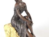 statue en bronze représentant une femme assise sur un rocher, sur fond blanc