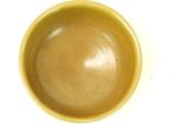 yellow bowl on a white table with a small amount of liquid in it