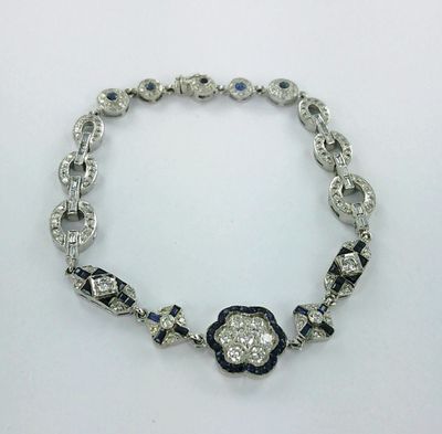 un gros plan d'un bracelet en diamants et saphirs posé sur une surface blanche