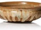 un bol en bois posé sur une surface blanche, à côté d'un vase