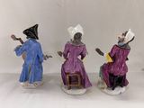three figurines of people dressed in purple and blue sitting on stools