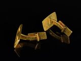 two gold cufflinks on a black surface with a black background