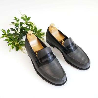 black leather loafers with gold buckles and a plant on a white surface