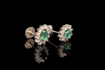 une paire de boucles d'oreilles en émeraude et diamant posées sur un fond noir
