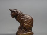 bronze statue of a cat sitting on a rock on a gray surface