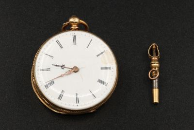 une montre de poche en or et une clé posées sur une surface noire