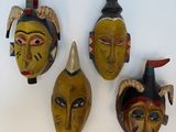 three wooden masks with horns and feathers on a white surface