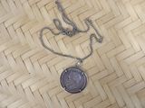 a necklace with a coin attached to it on a woven surface