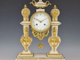 une horloge blanche et dorée posée sur un socle, sur fond gris