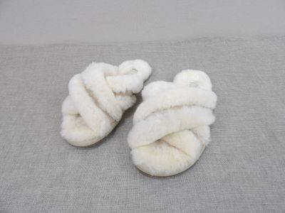 une paire de chaussons blancs ornés d'un nœud, posés sur un fond gris