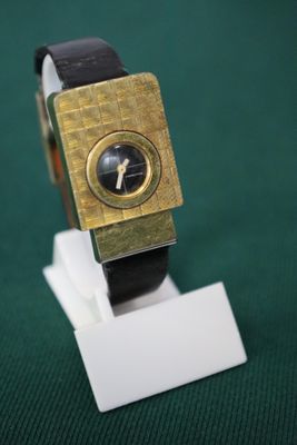 a gold watch on a white stand on a green surface