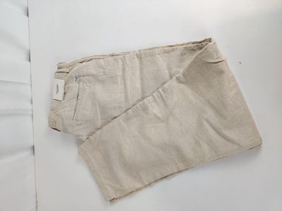 un pantalon beige posé sur un lit recouvert de draps blancs et d'un oreiller blanc