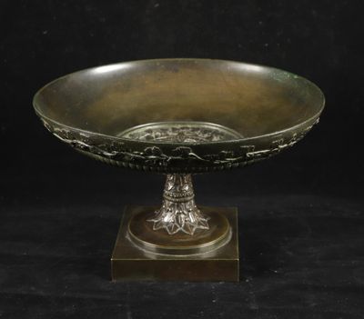 un bol antique en bronze posé sur un socle en bois, sur fond noir