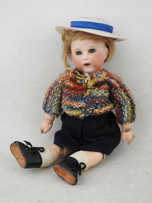 une poupée assise par terre, coiffée d'un chapeau