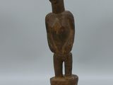 une statue en bois représentant un homme tenant un bol, posée sur un socle noir
