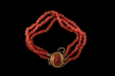 un gros plan sur un bracelet en perles rouges muni d'un fermoir doré