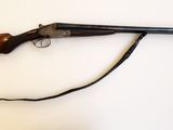 un vieux pistolet avec une crosse en bois et une sangle, posé sur une surface blanche