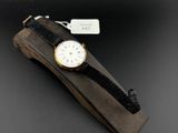 une image représentant une montre posée sur un socle en bois, sur une surface noire