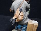 figurine of a man sitting on a bench with a bag and a suitcase