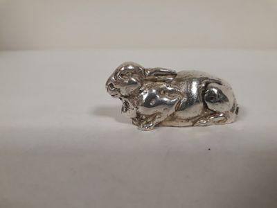 une image représentant une figurine en argent en forme de chien posée sur une surface blanche