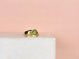 une bague en or sertie d'un péridot posée sur un bloc de marbre