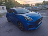 a blue car parked in a parking lot with a sunset in the background