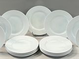 twelve white dinner plates stacked on top of each other on a table